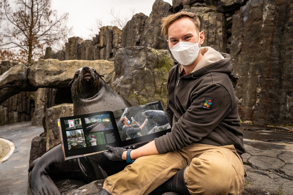 Kniha Ztichlá zoo umožní návštěvníkům nahlédnout do doby, kdy byla Zoo Praha sice uzavřená, ale žila dál. Prostřednictvím fotografií vás zavede do zákulisí práce chovatelů a mezi zvířata, která jste vidět nemohli. Na snímku vrchní chovatel Jakub Mezei se samcem lachtana jihoafrického Melounem. Autor: Oliver Le Que, Zoo Praha 